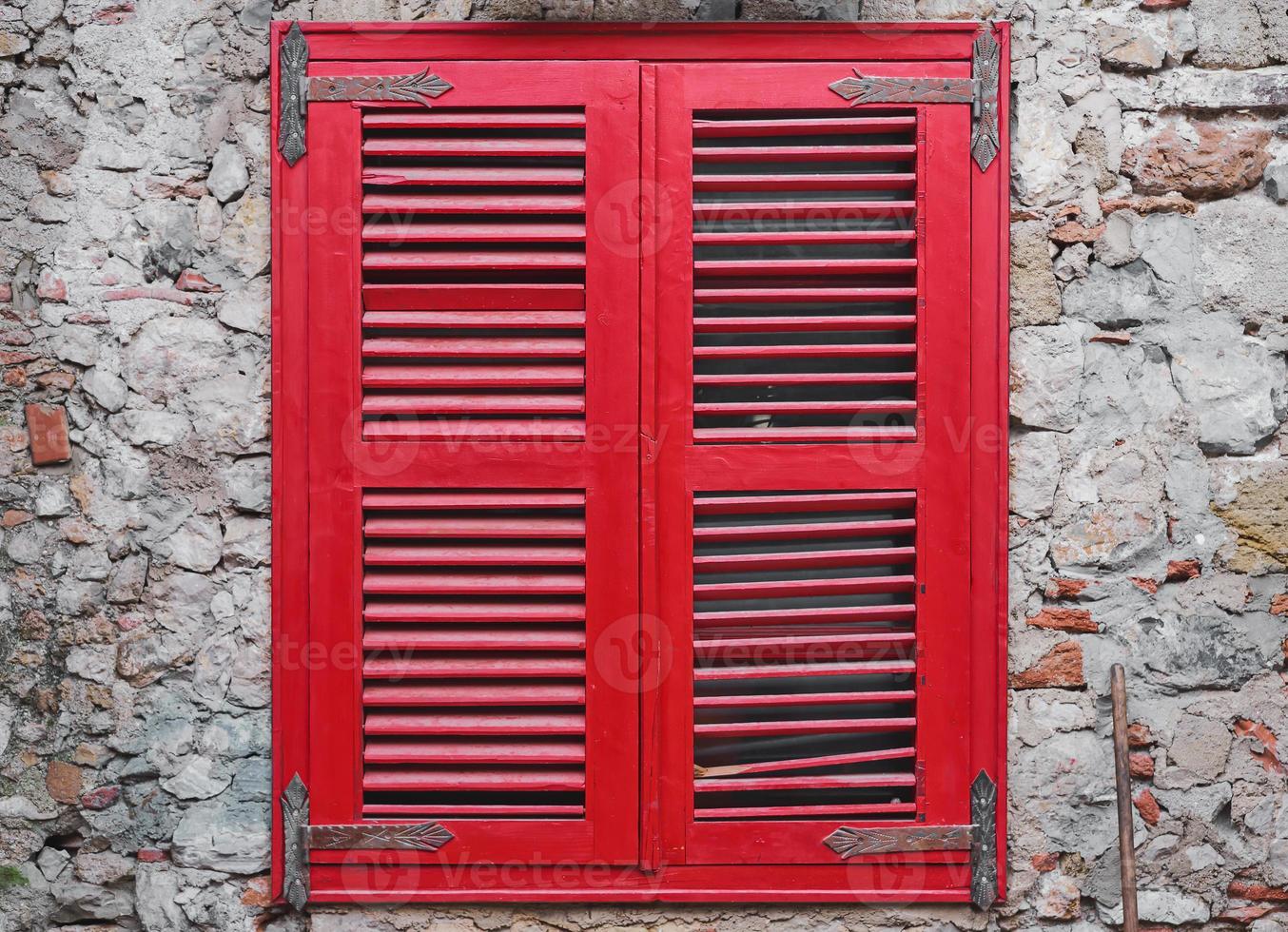 Red wooden blinds close the window on the old stone wall of the house. Old brick wall, idea for interior or loft studio and courtyard photo