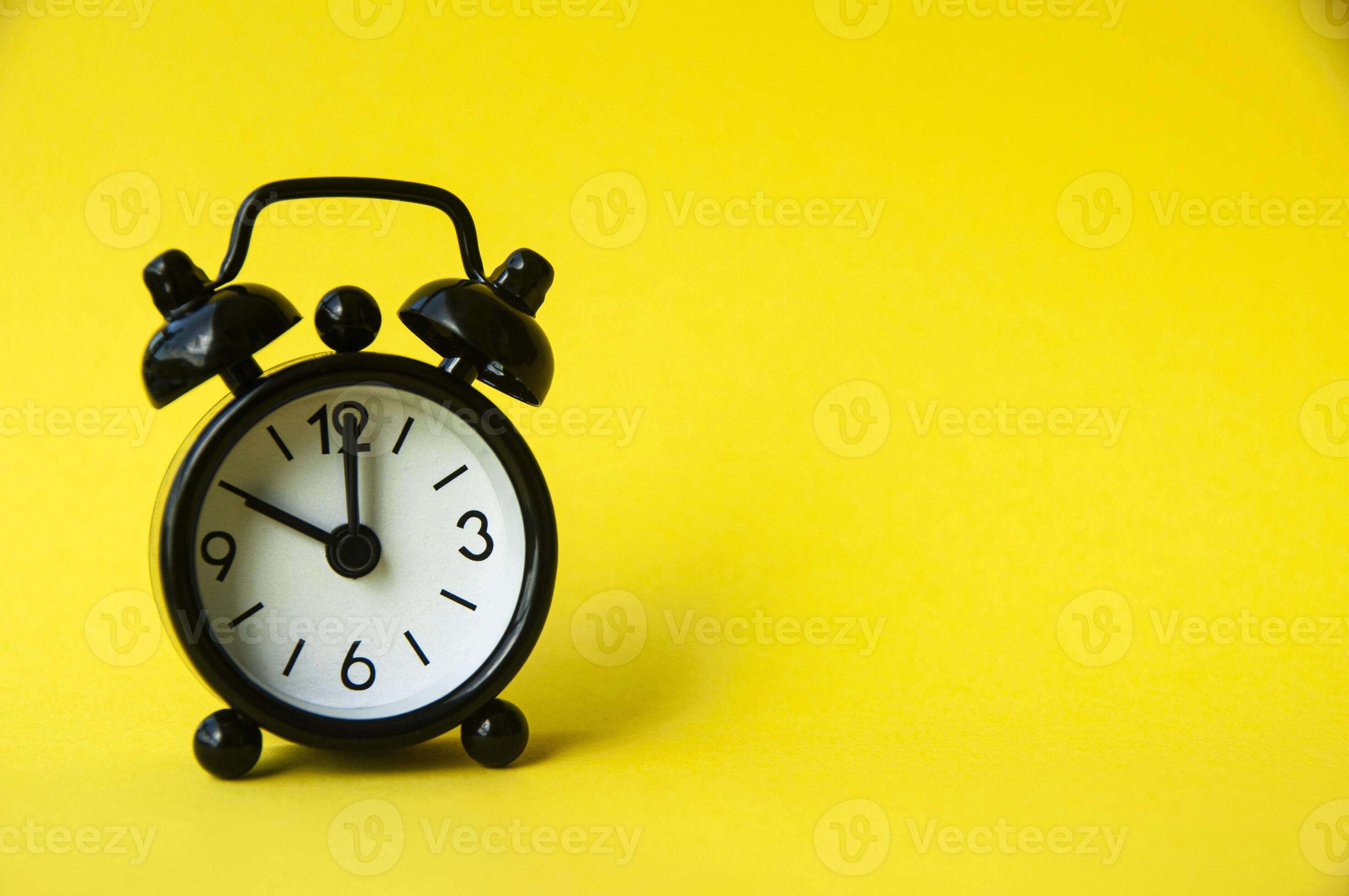 Black alarm clock isolated on yellow background. The clock set at 10 o