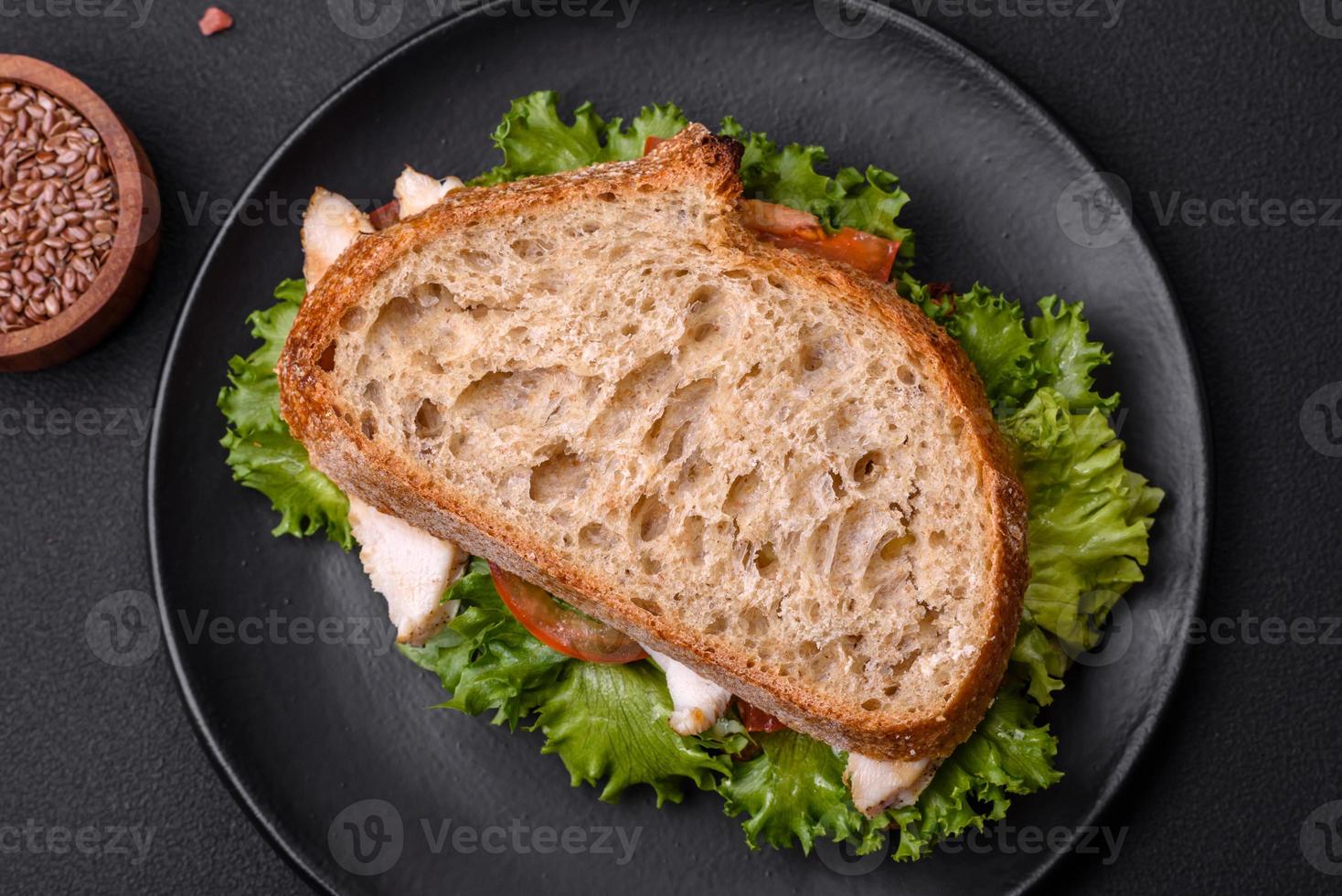 Fresh tasty sandwich with chicken, tomatoes and lettuce on a black plate photo
