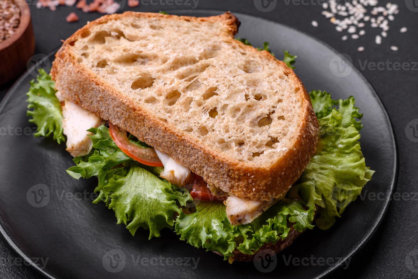 Sándwich fresco y sabroso con pollo, tomates y lechuga en un plato negro foto