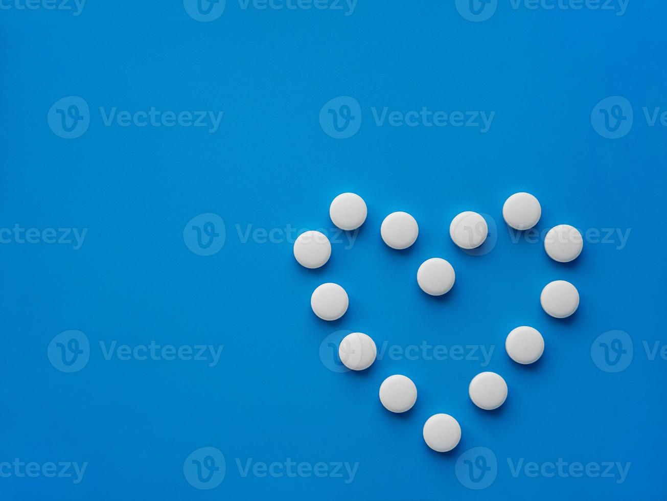 Medications tablets are laid out in the shape of a heart on a blue background. The concept of treatment of heart disease photo
