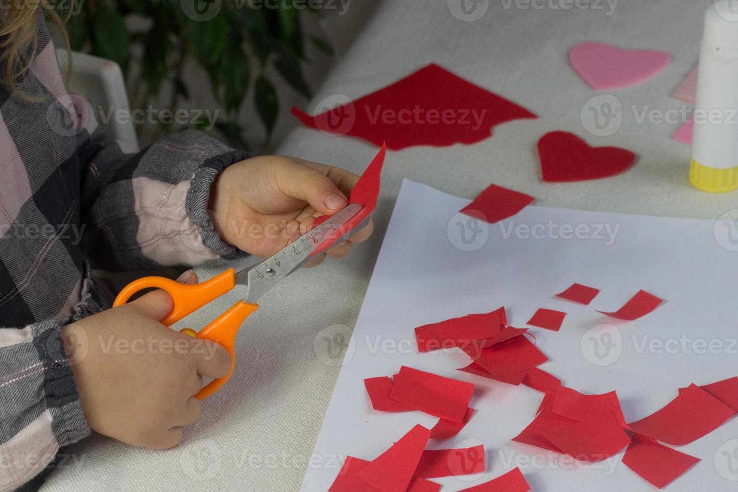 Little girl making red heart applique with paper and glue on white sheet,Valentines Day greeting card, holiday gift for Mothers day,hand made kids present,love symbol with paper,toddler activity photo