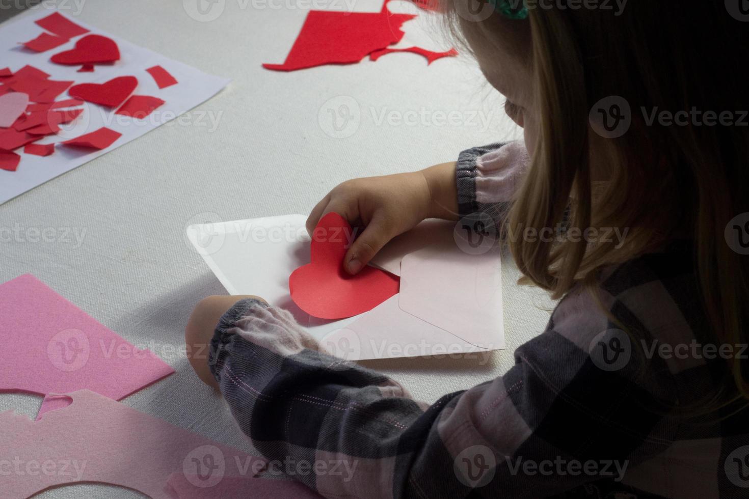 niño con carta con corazón de papel rojo, carta de amor para el día de san valentín, regalo para el día de la madre, niña pequeña que puso el corazón hecho a mano dentro del sobre, saludos navideños de la hija, maqueta para deseos de amor foto