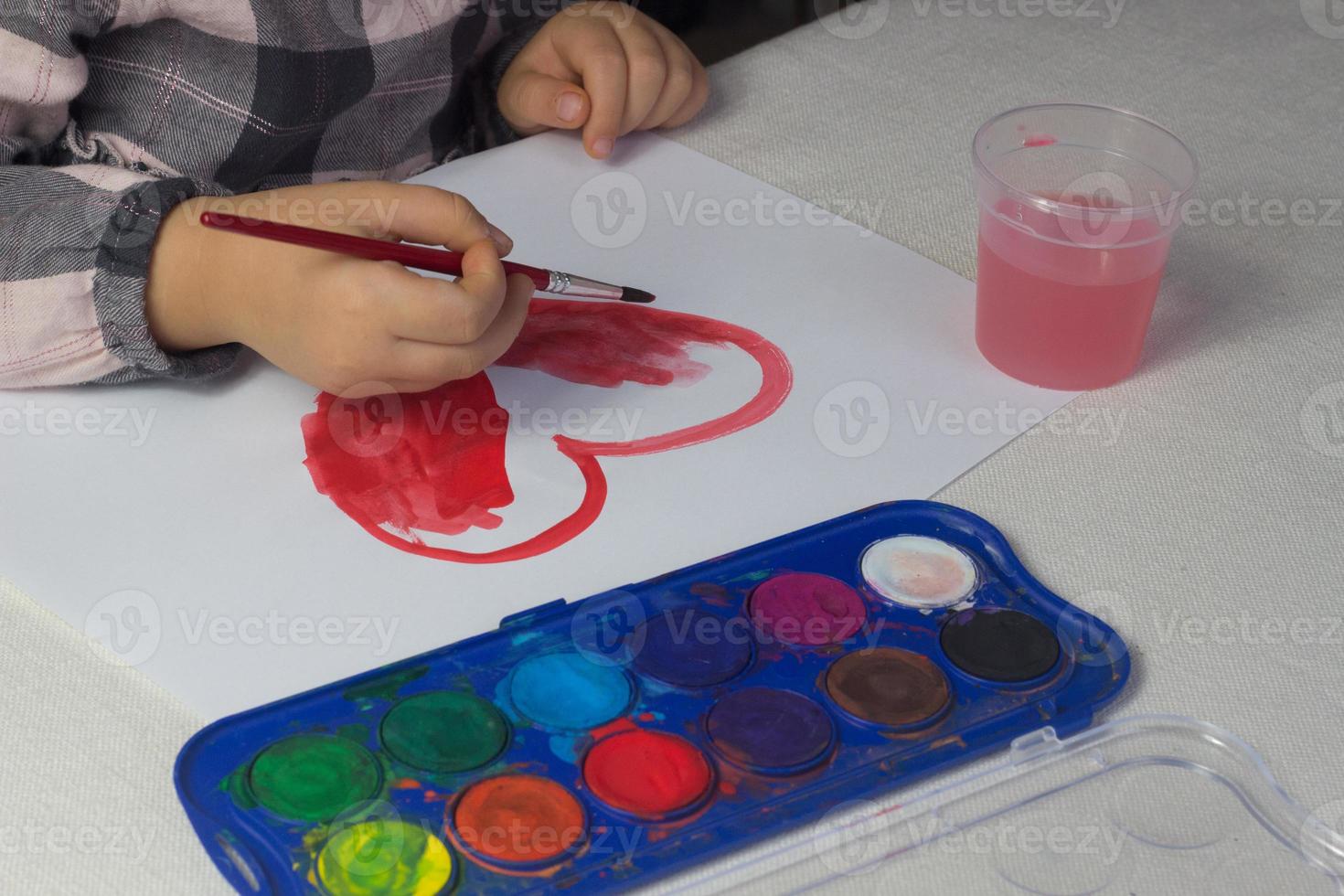 Little girl sitting at the table and drawing red heart watercolor,Valentine day postcard,greeting card,art school concept,advertising,child painting watercolor at home,toddler activity,kids leisure. photo