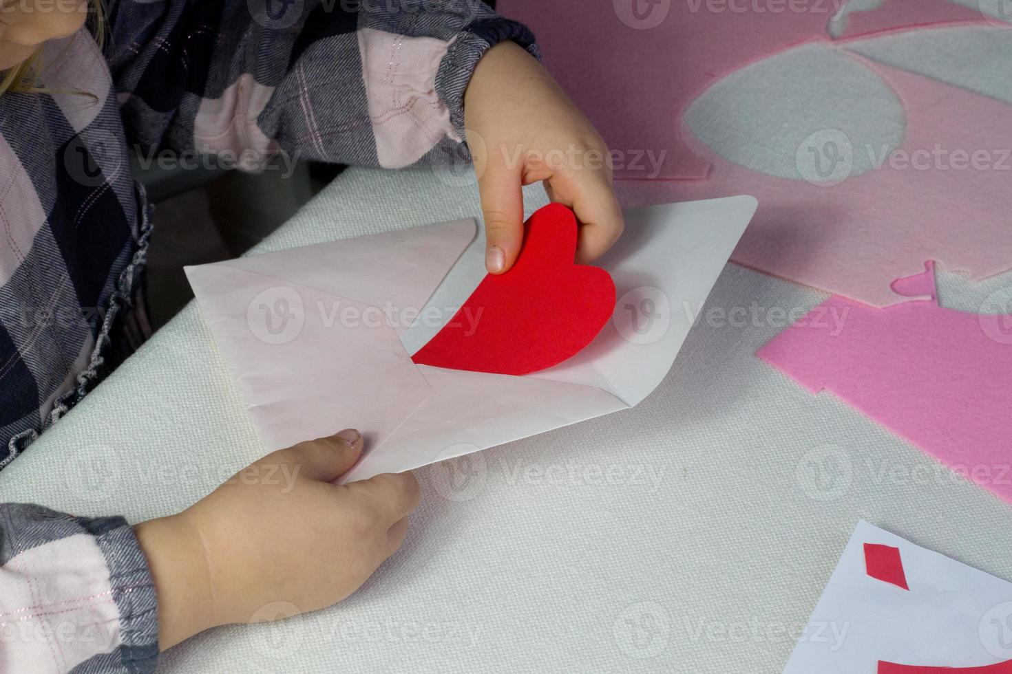 niño con carta con corazón de papel rojo, carta de amor para el día de san valentín, regalo para el día de la madre, niña pequeña que puso el corazón hecho a mano dentro del sobre, saludos navideños de la hija, maqueta para deseos de amor foto