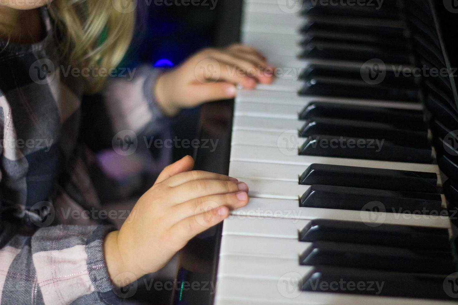 niña pequeña toca el piano, los niños manos en el teclado del piano de cerca, educación en el hogar, educación musical. niño talentoso en crecimiento. rutina diaria para niños pequeños, vista lateral de las manos y el piano de los niños. foto