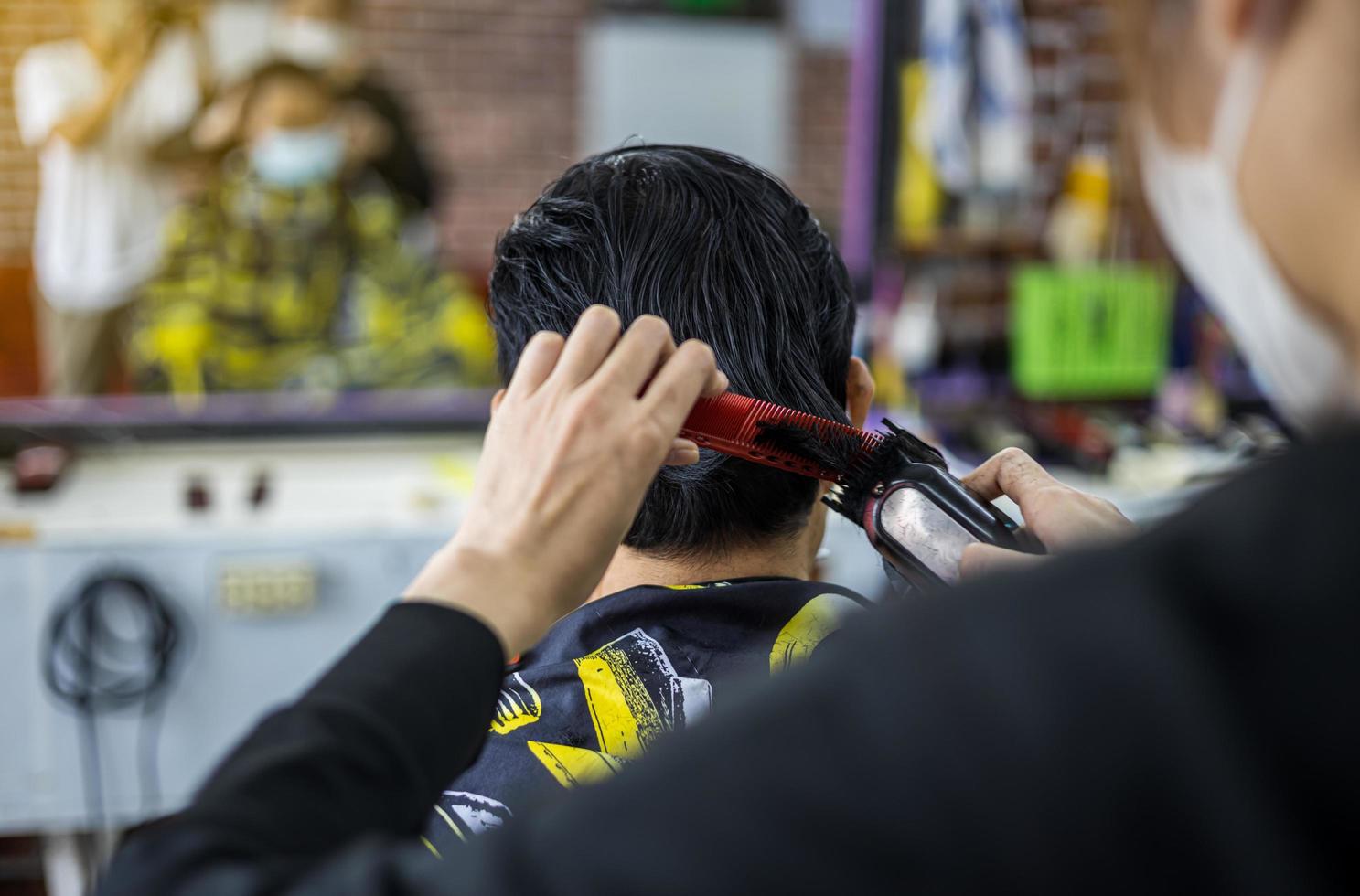 A close-up view of a man's back is a masked barber woman using a comb and clippers. photo