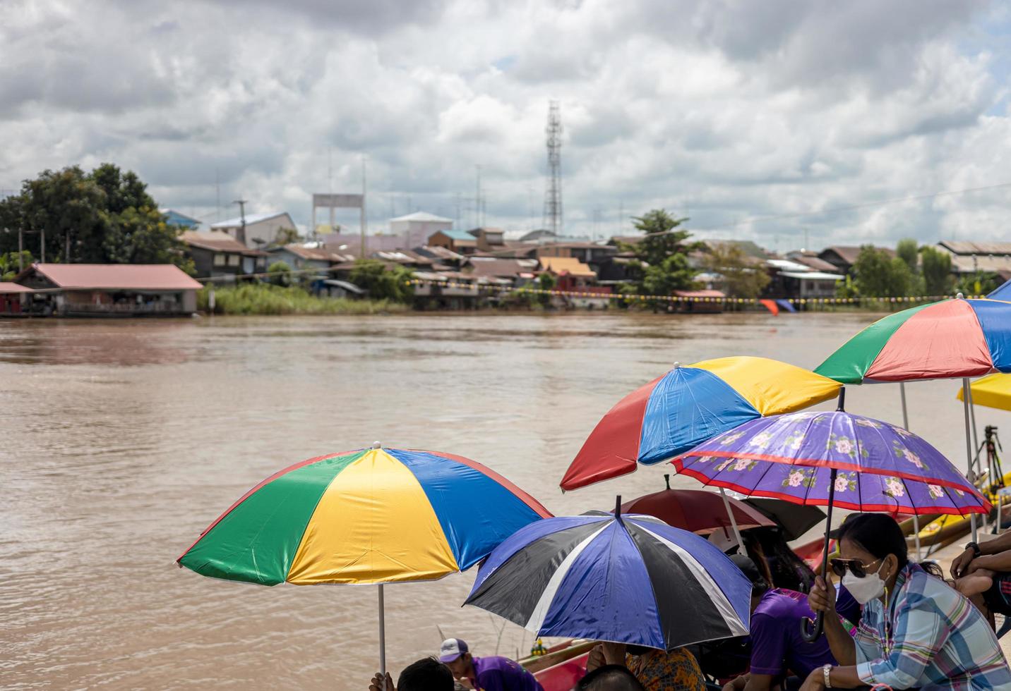 A close-up view of colorful umbrellas with people spreading their shade on the riverbank. photo