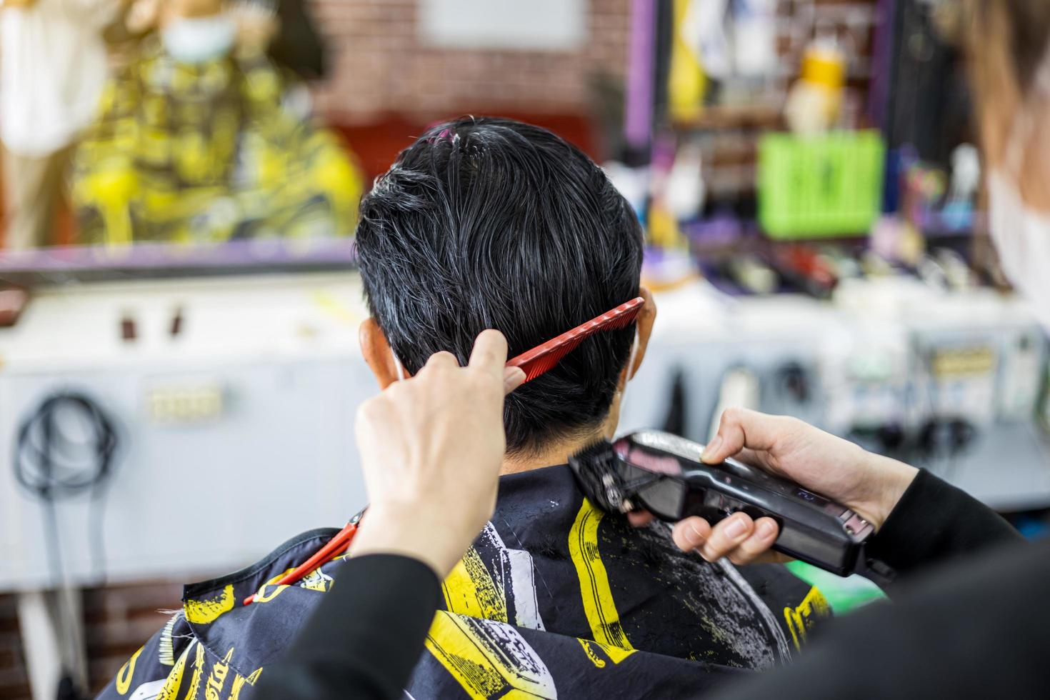 A close-up view of a man's back is a masked barber woman using a comb and clippers. photo