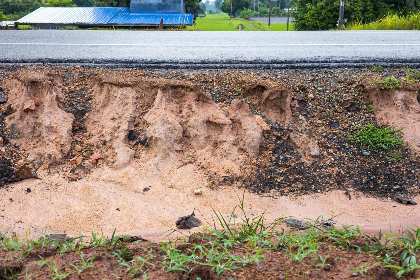 A side view of the sandstone soil beneath an asphalt road eroded by rain and wild water. photo