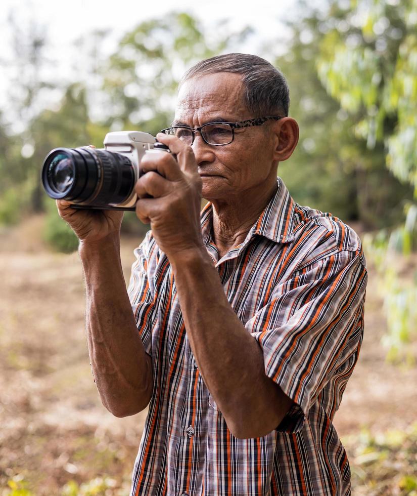 retrato de un anciano tailandés con gafas sosteniendo una vieja cámara dslr. foto