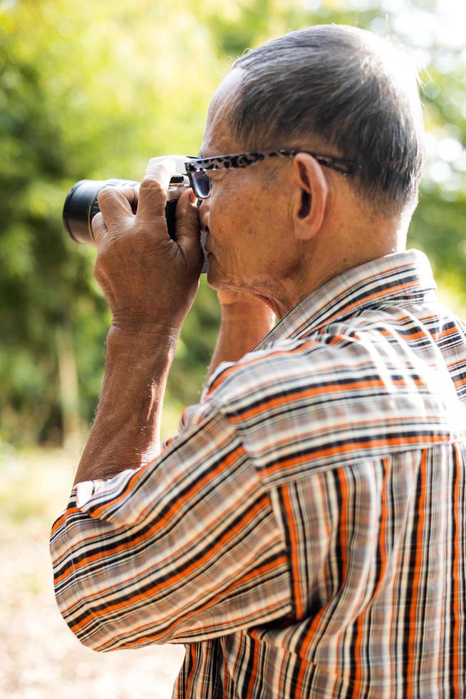 toma lateral de un anciano tailandés con gafas sosteniendo una vieja cámara dslr. foto