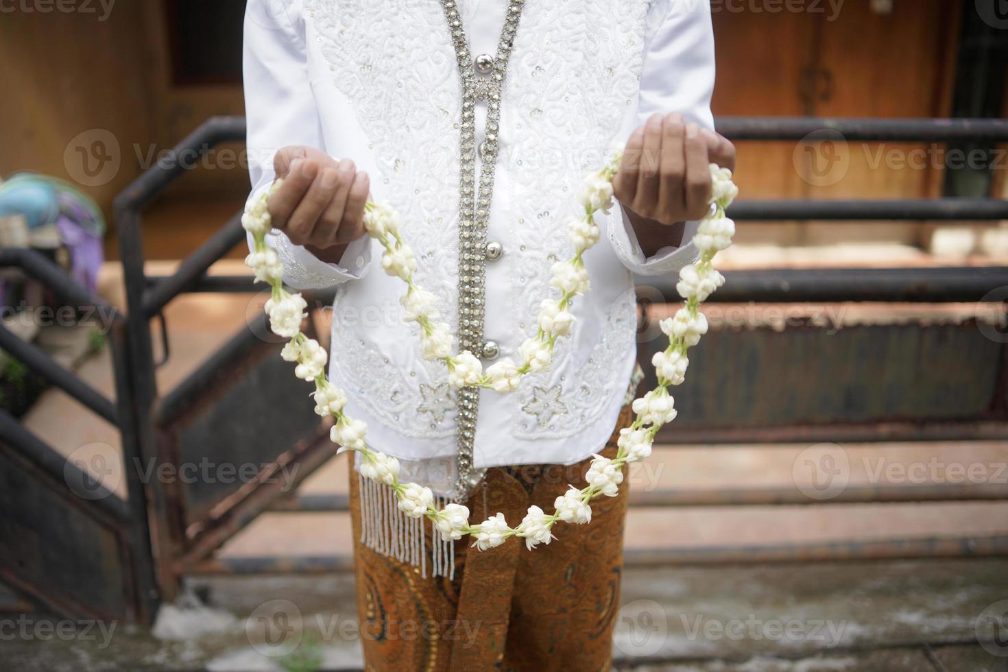 Beautiful Groom Holding Jasmine and Magnolia Flower Necklace for a Traditional Wedding Ceremony in Indonesia photo