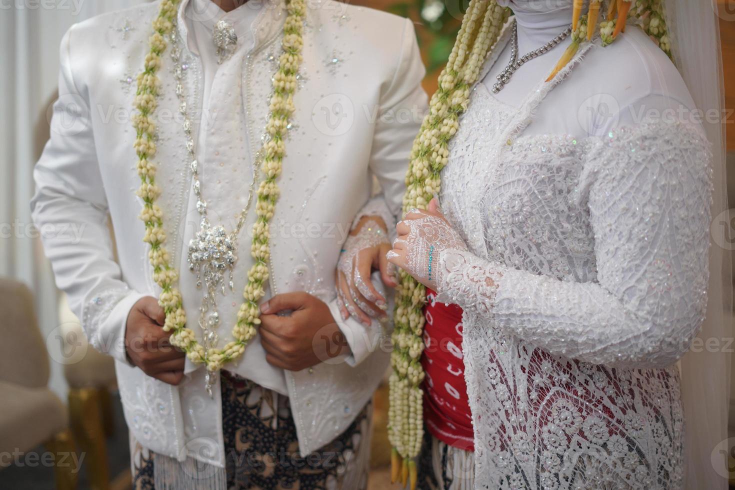 Beautiful Bride and Groom Standing while Wearing Wedding Dress with Jasmine and Magnolia Flower Necklace for a Traditional Wedding Ceremony in Indonesia photo