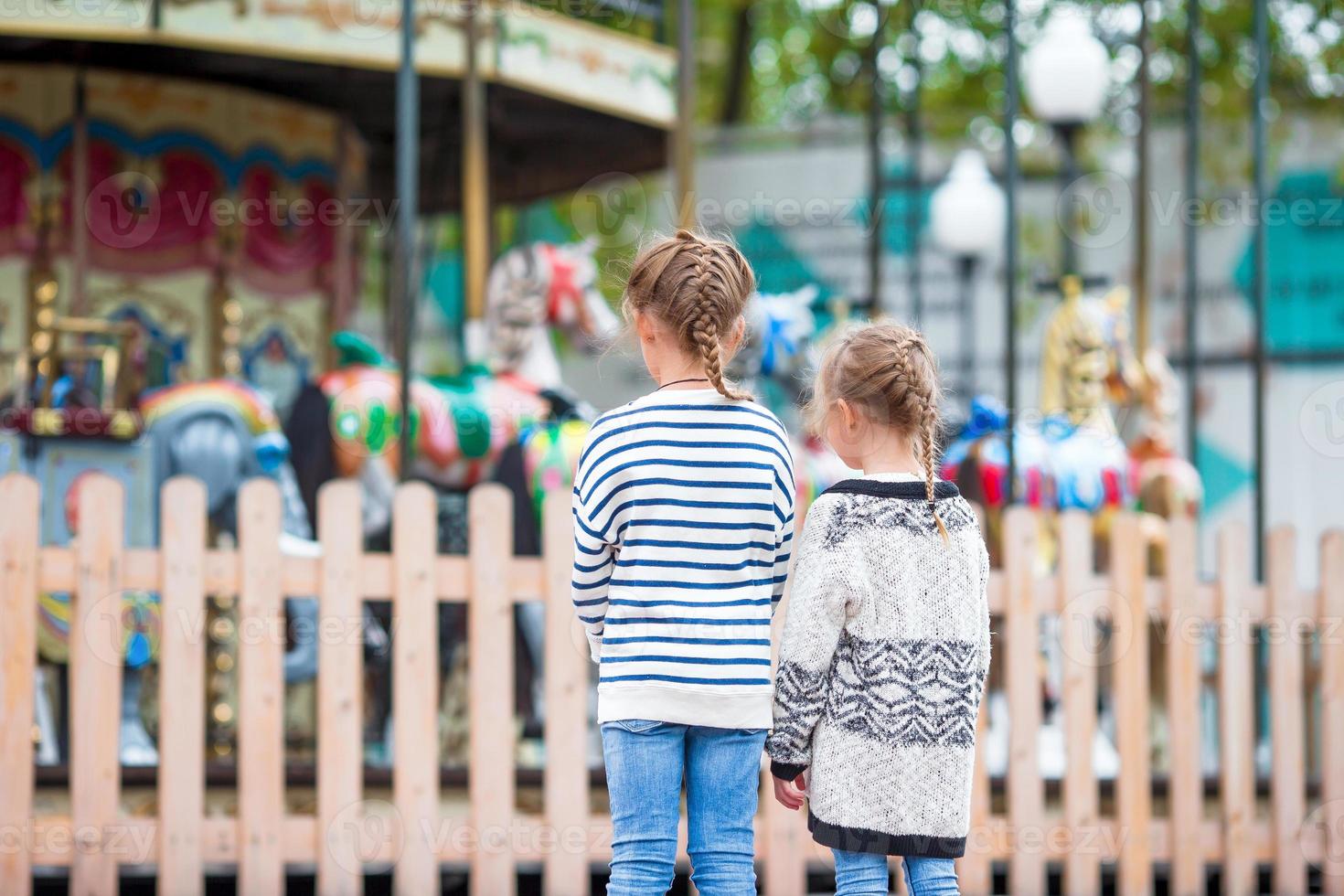 Adorable little girls near the carousel in the kids park outdoors photo