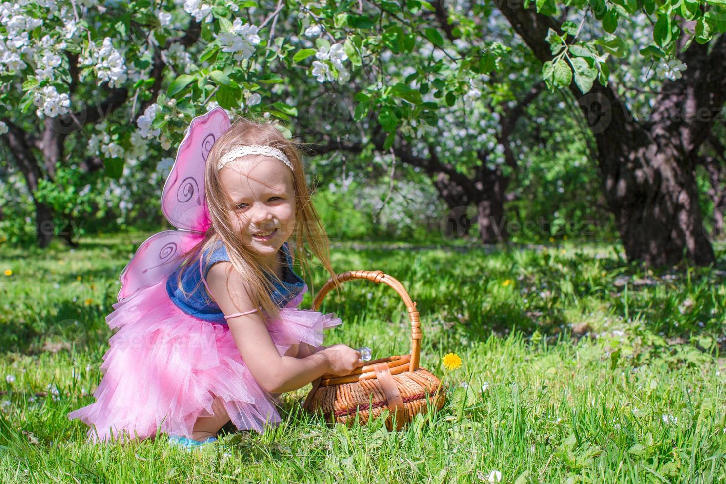 Adorable little girl with straw basket in blossoming apple orchard photo