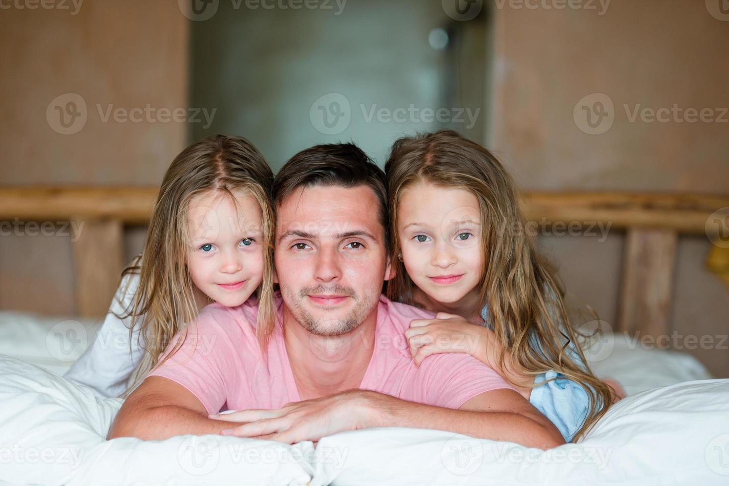 padre con dos niñas adorables divirtiéndose en la cama sonriendo foto