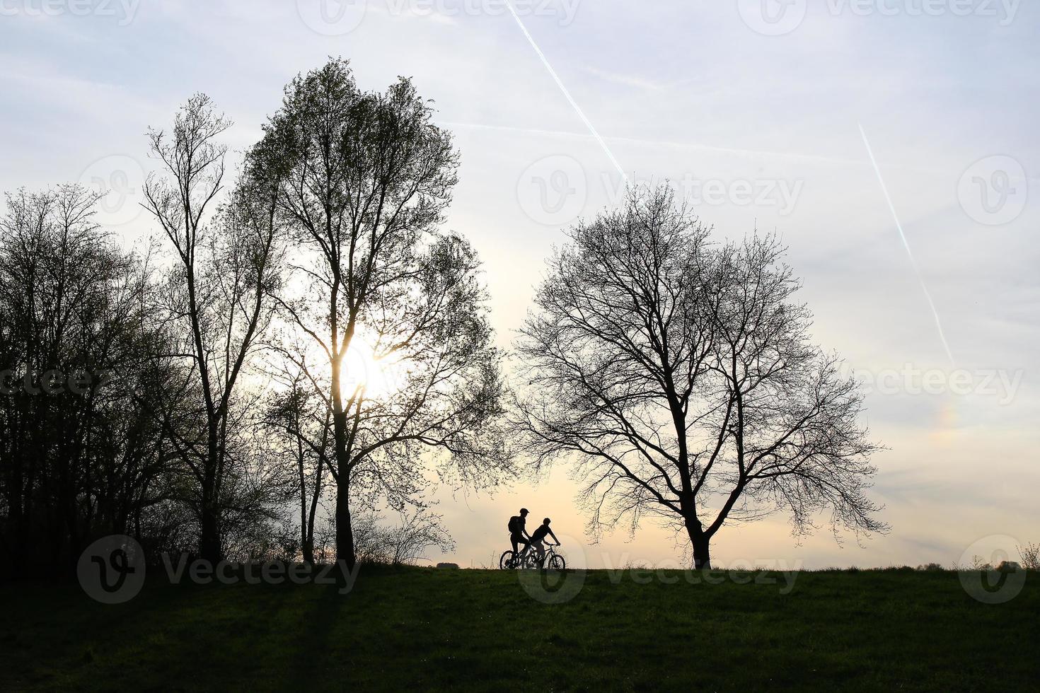 silueta de personas montando en bicicleta en un camino rural al atardecer a lo largo del río danubio en regensburg, alemania, europa. foto