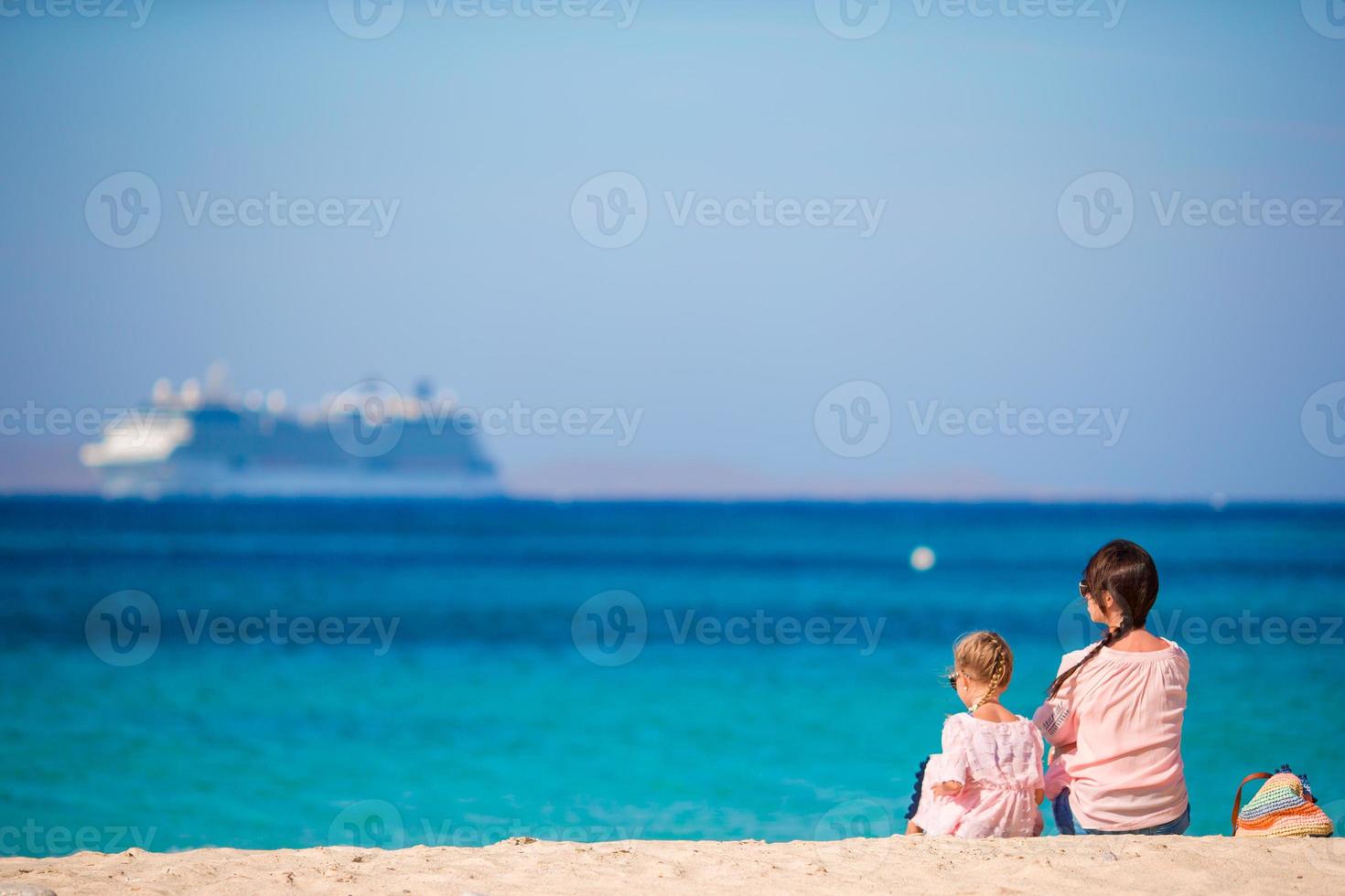 Young mom and adorable girl at beach on sunny day with view of big liner photo