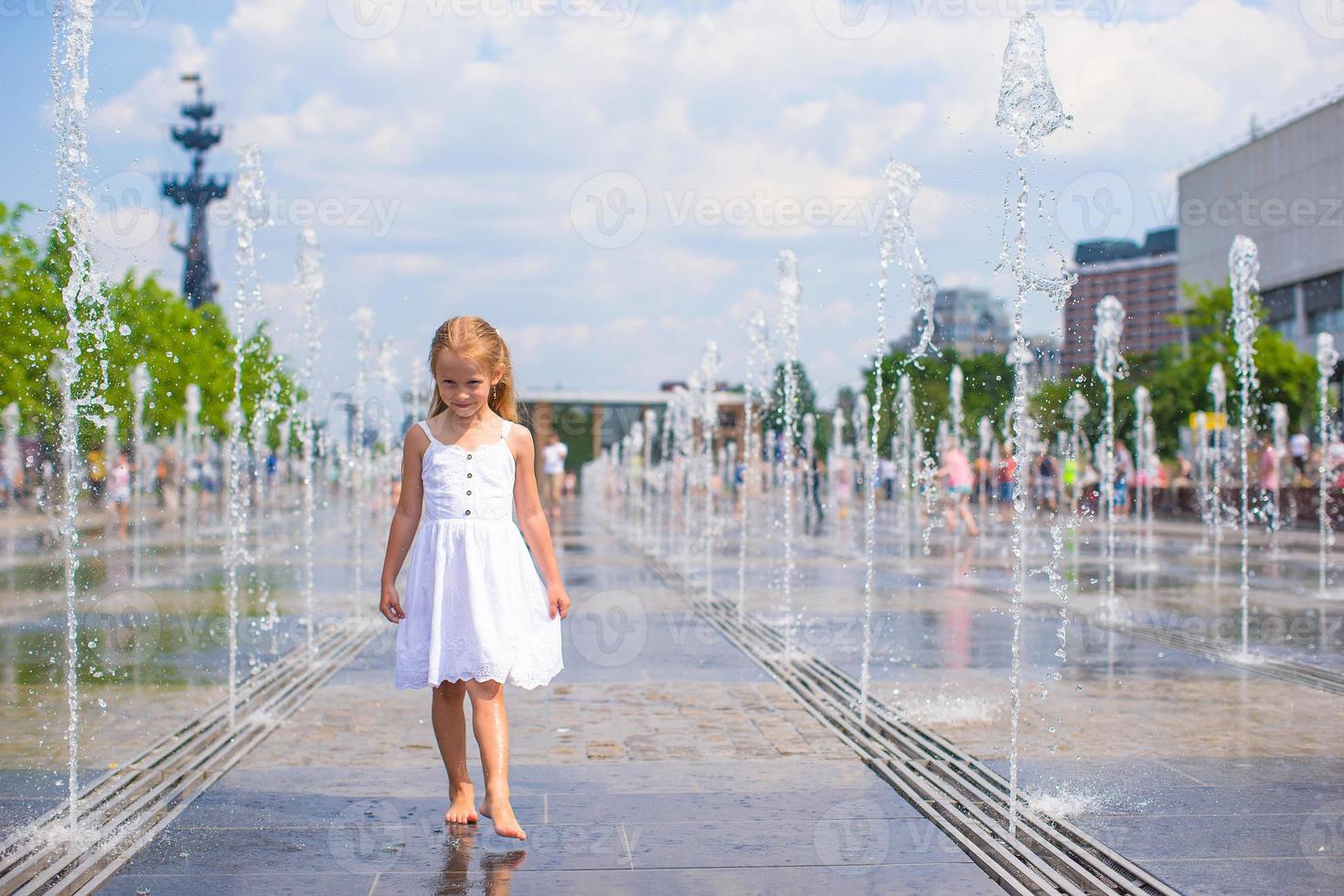 Cute girl having fun in outdoor fountain at hot day photo