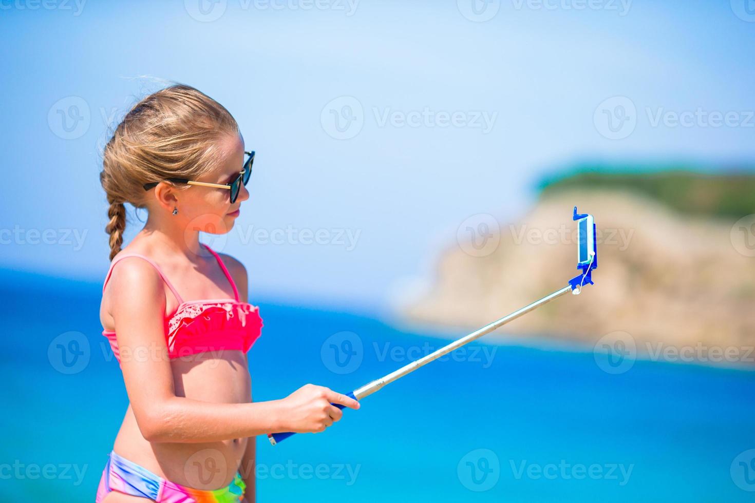 Little girl taking selfie by her smartphone on the beach. Kid enjoying her suumer vacation and making photos for memory