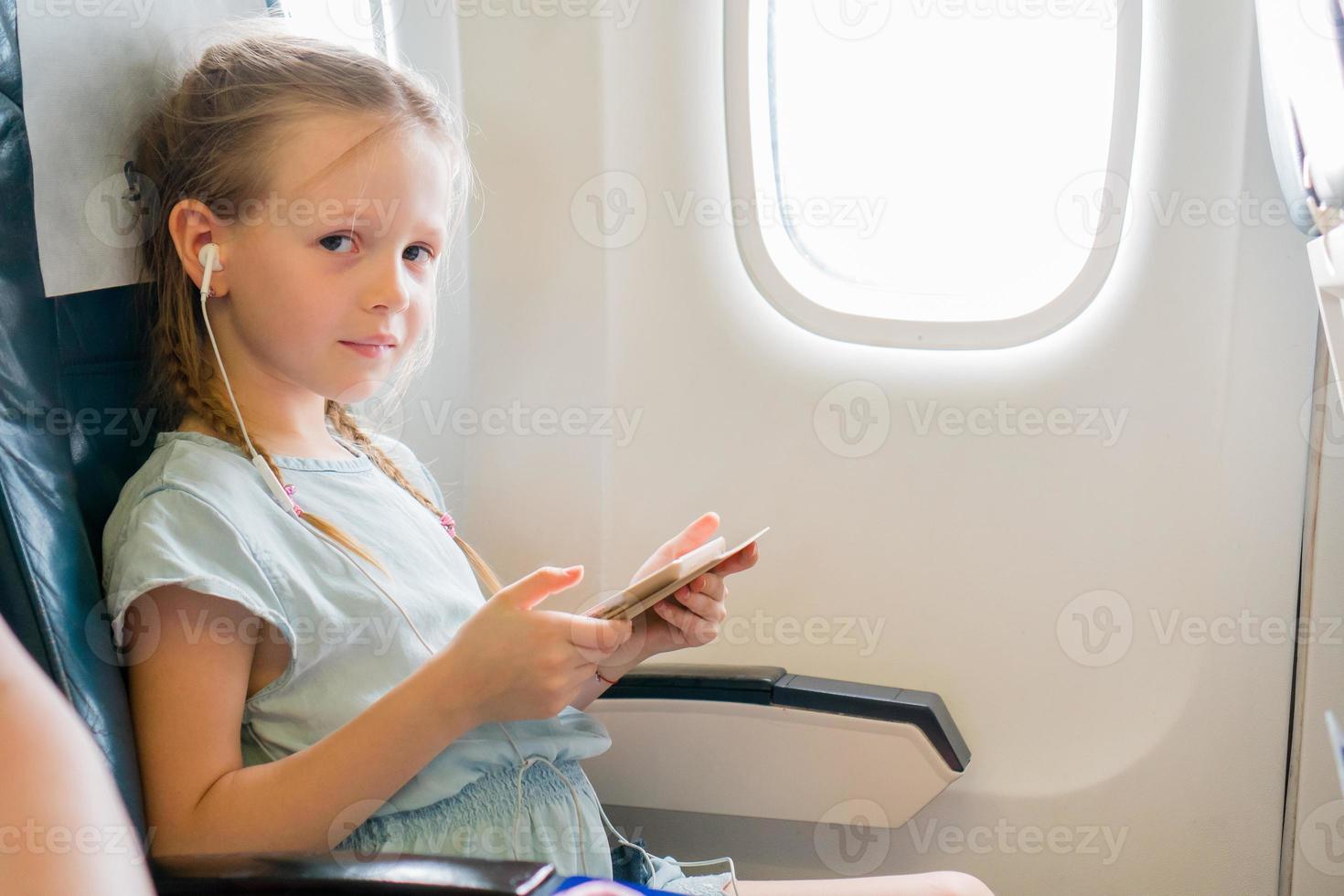 Adorable little girl traveling by an airplane. Cute kid with laptop near window in aircraft photo