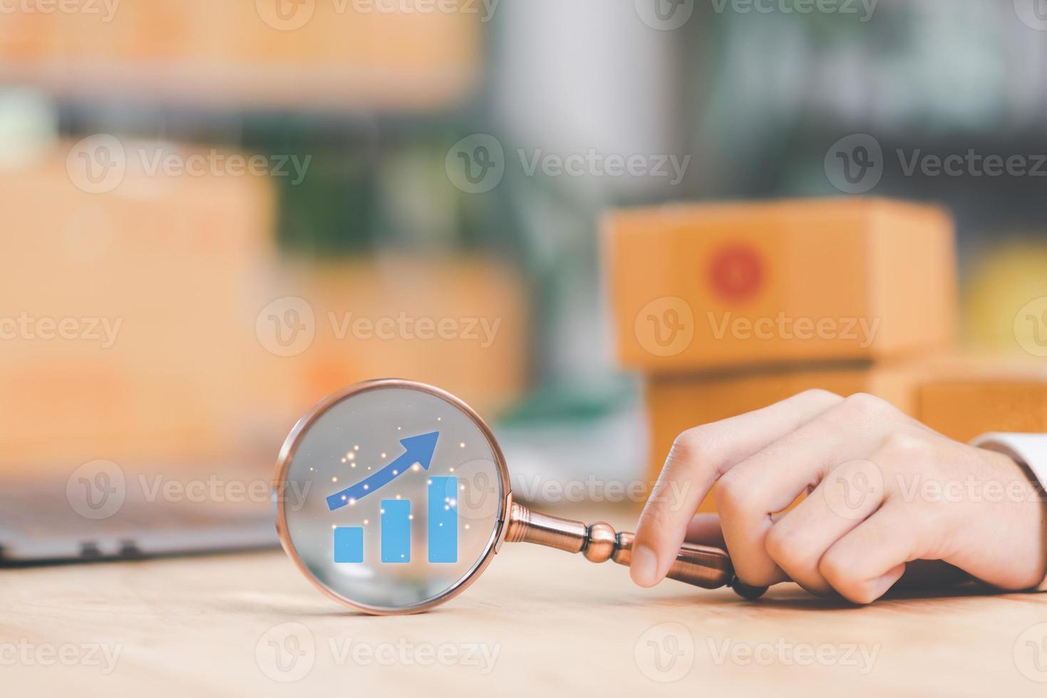 Startup or small business entrepreneur holding a magnifying glass, business growth graph, internet shopping, internet online shopping, SME, delivery box, e-commerce,business goal setting photo