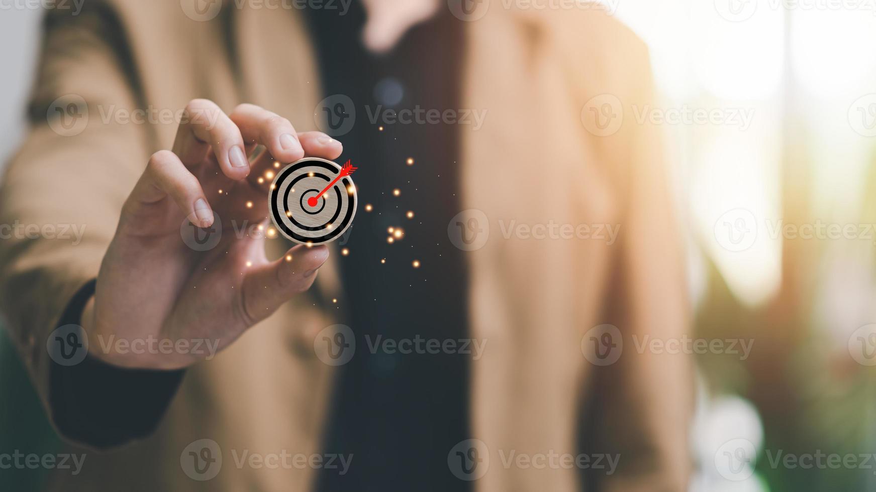 Wooden block in businessman hand and arrow icon hitting center of dartboard target,Setting business goals and focused concepts, Organizational growth and objectives, marketing strategy planning photo