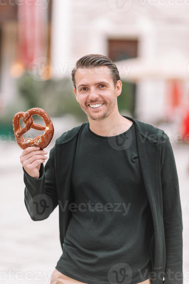 Beautiful young man holding pretzel and relaxing in park photo