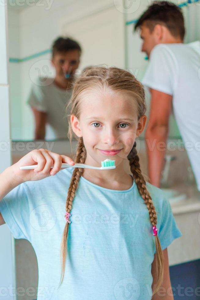 Little beautiful girl with white teeth and her young father brushing teeth in the bathroom photo