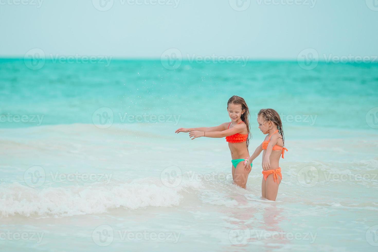 Little girls having fun at tropical beach playing together at shallow water photo