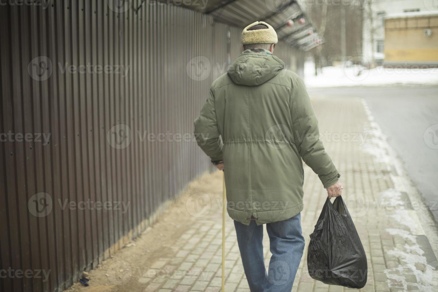 Old man walks with bag of groceries. Pensioner in Russia. Man walks down street. photo