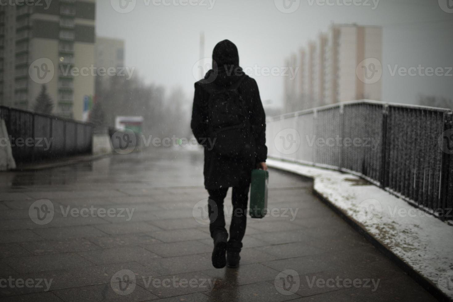 Guy with diplomat walks down street. Man in black clothes in city. Cloudy weather in afternoon. photo