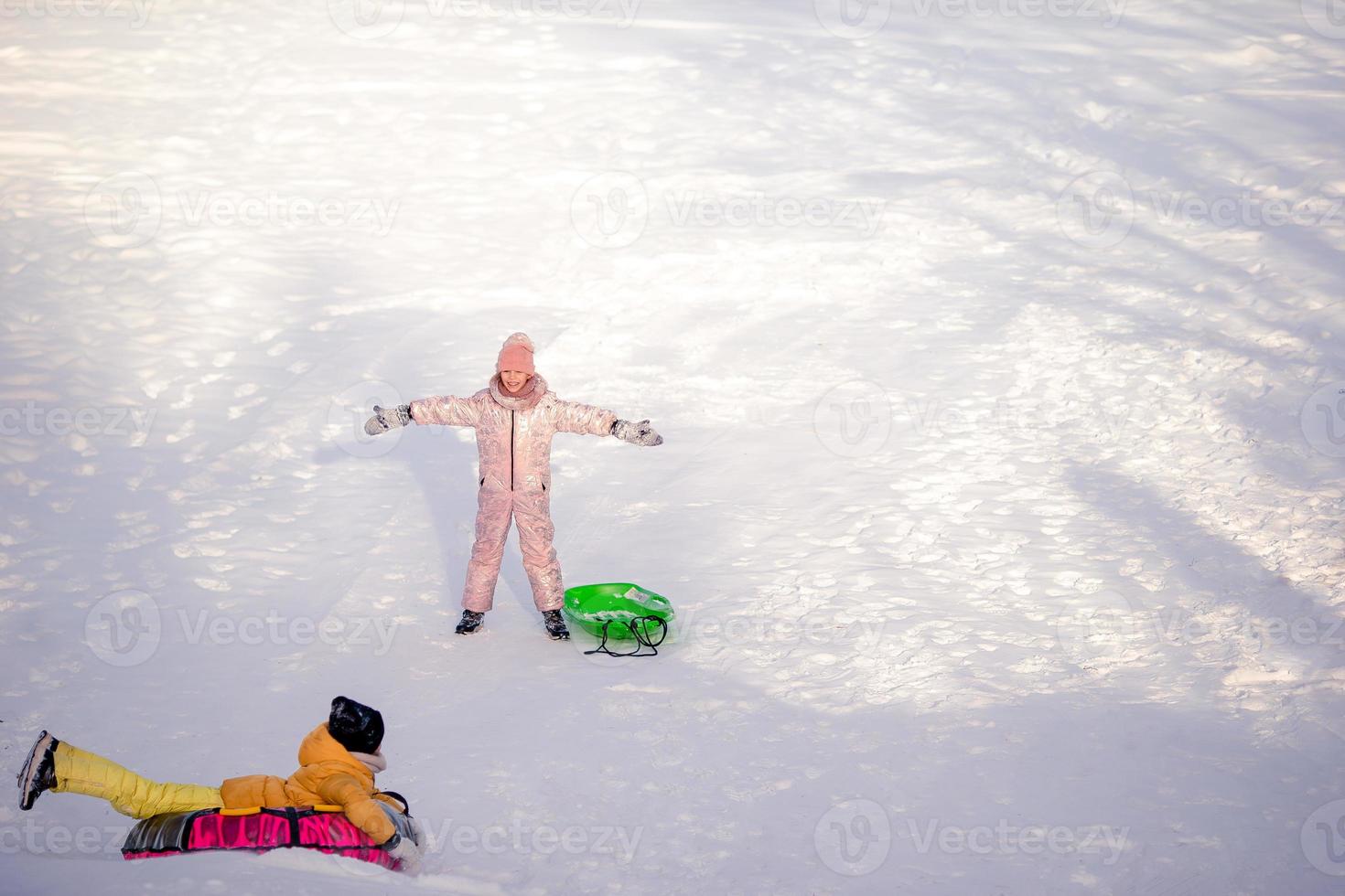 Adorable little happy girls sledding in winter snowy day. photo