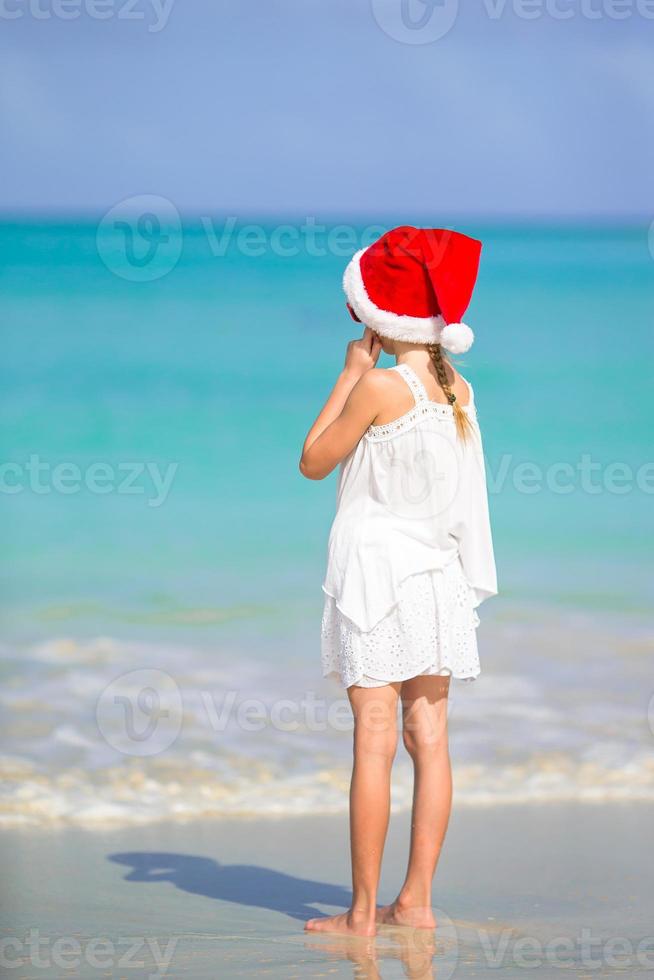 Adorable little girl in Santa hat on tropical beach photo