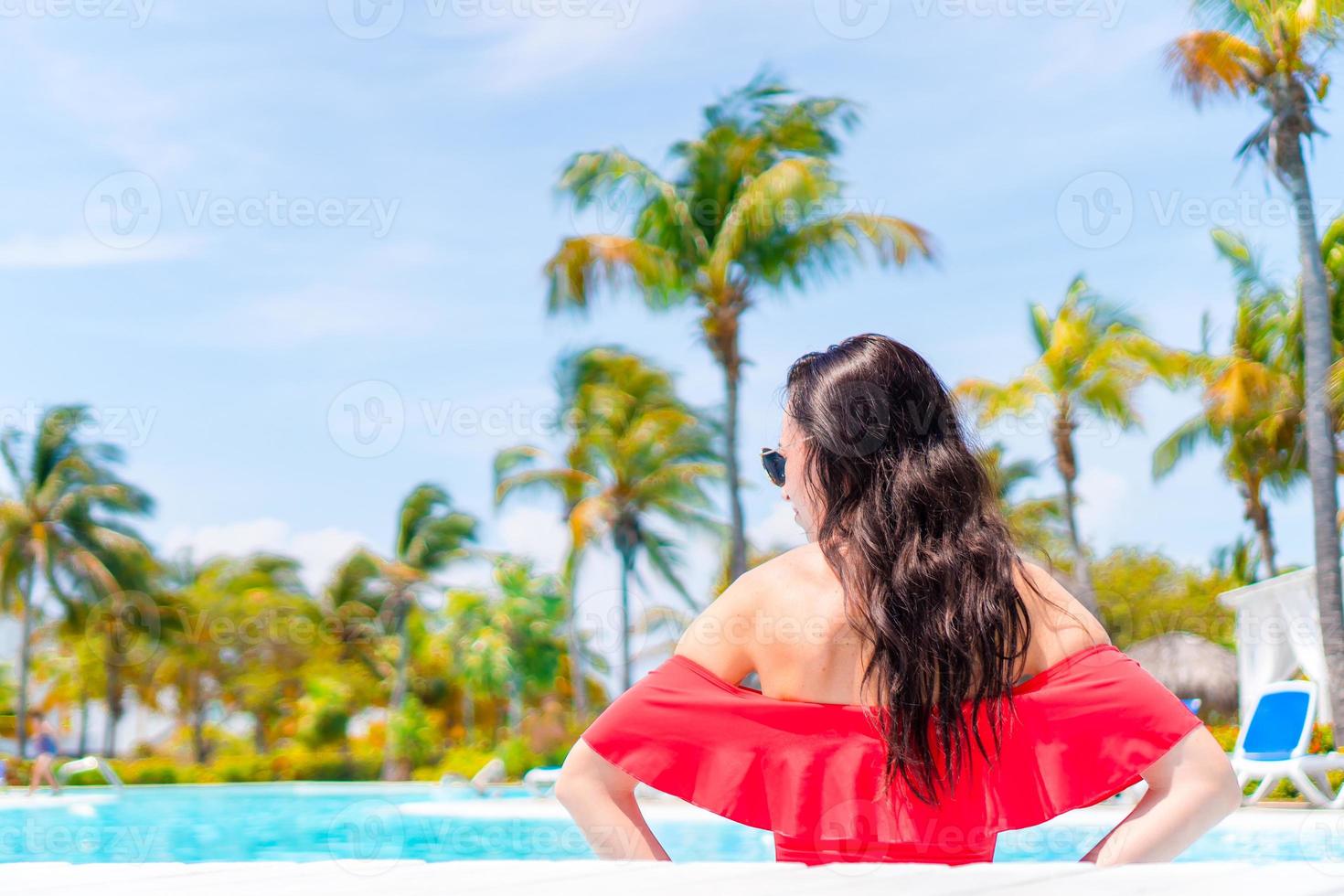 Beautiful young woman relaxing in swimming pool. Girl in red bikini in outdoor pool at luxury hotel photo