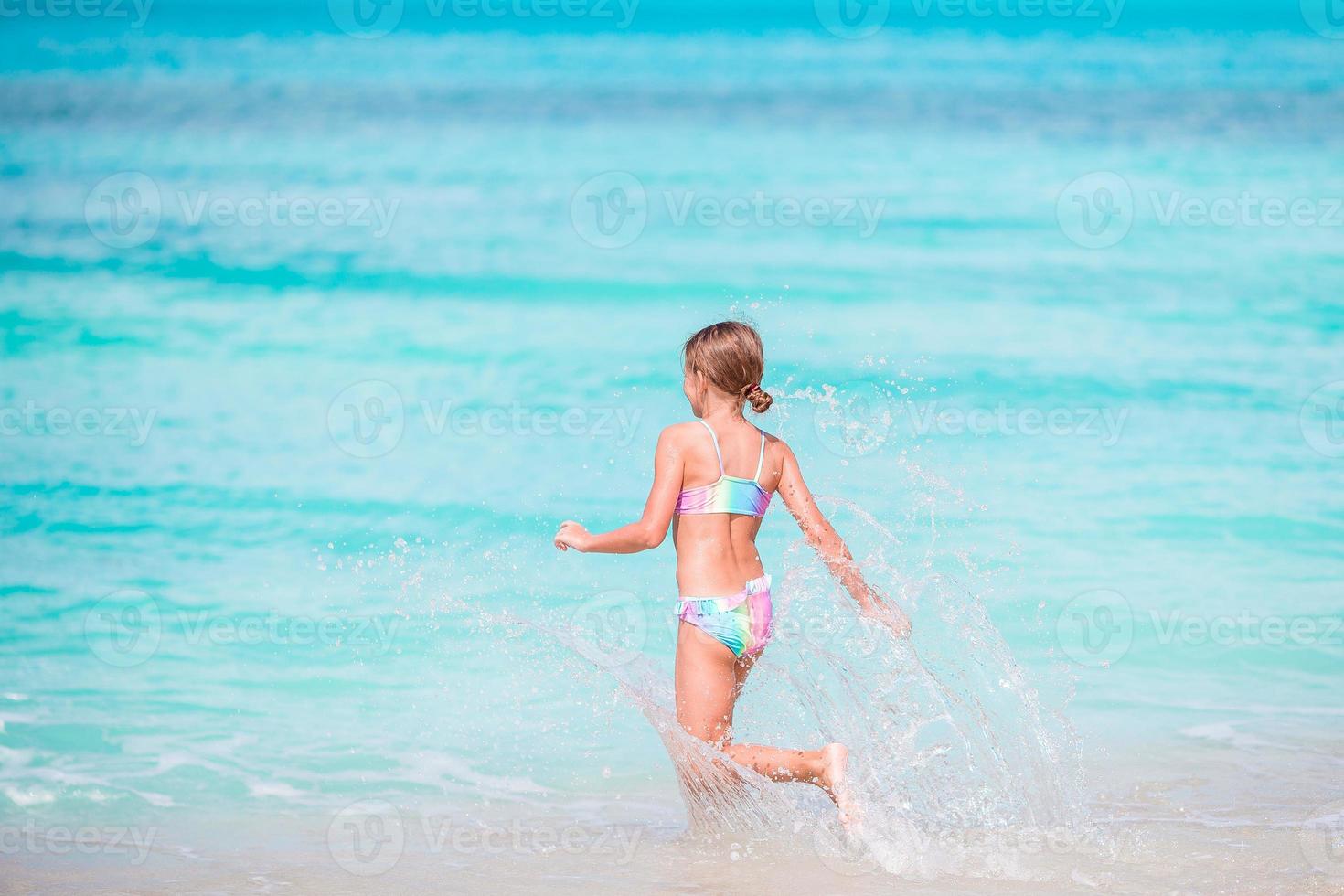 Little happy girl splashing. Kid running to the turquoise water ready to swim photo