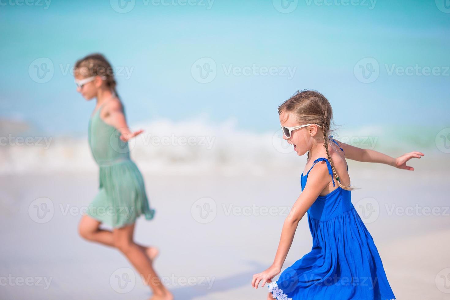 Adorable little girls have a lot of fun on the beach. Two beautiful kids running and splashing in shallow water photo