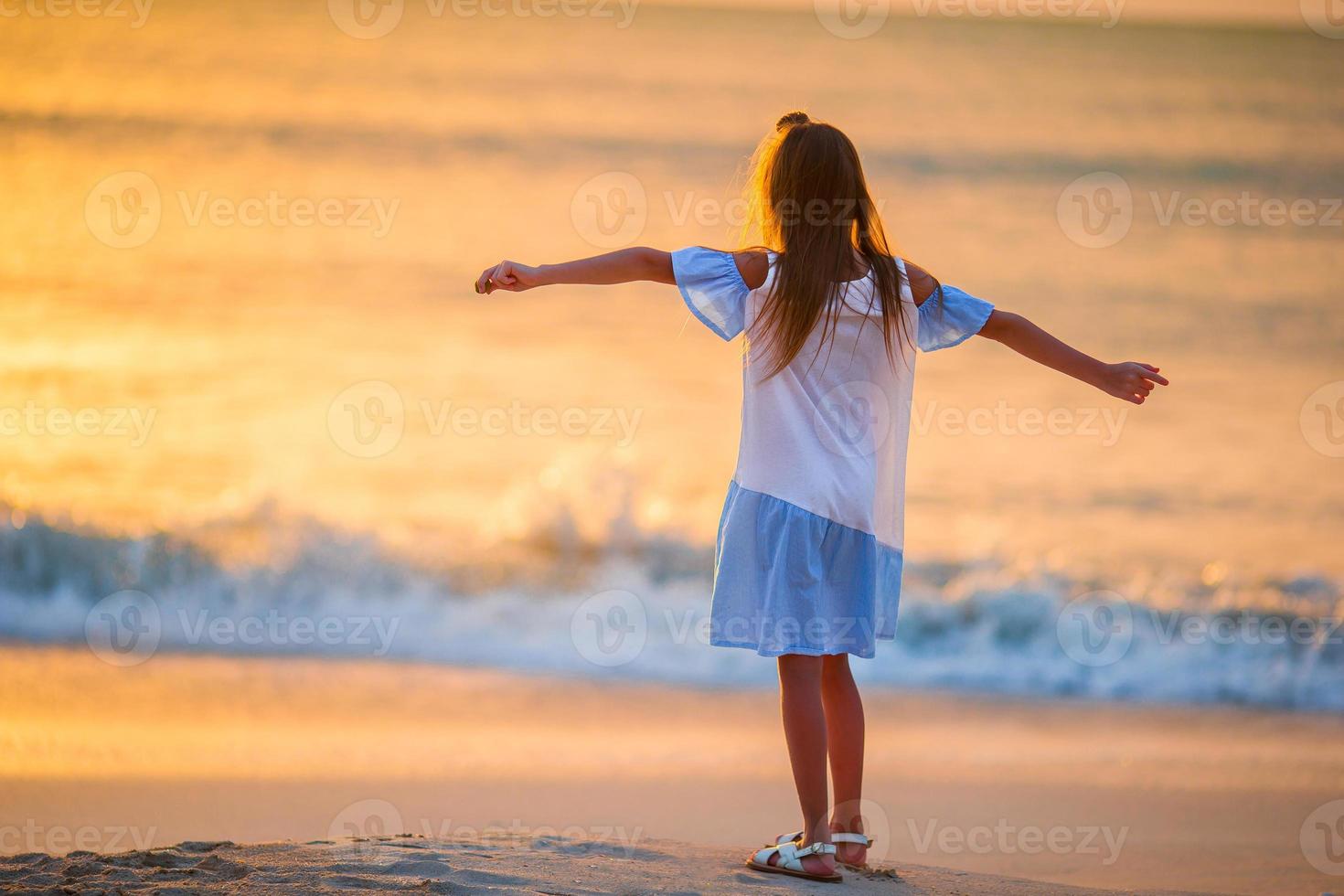 adorable niña feliz caminando en la playa blanca al atardecer. foto