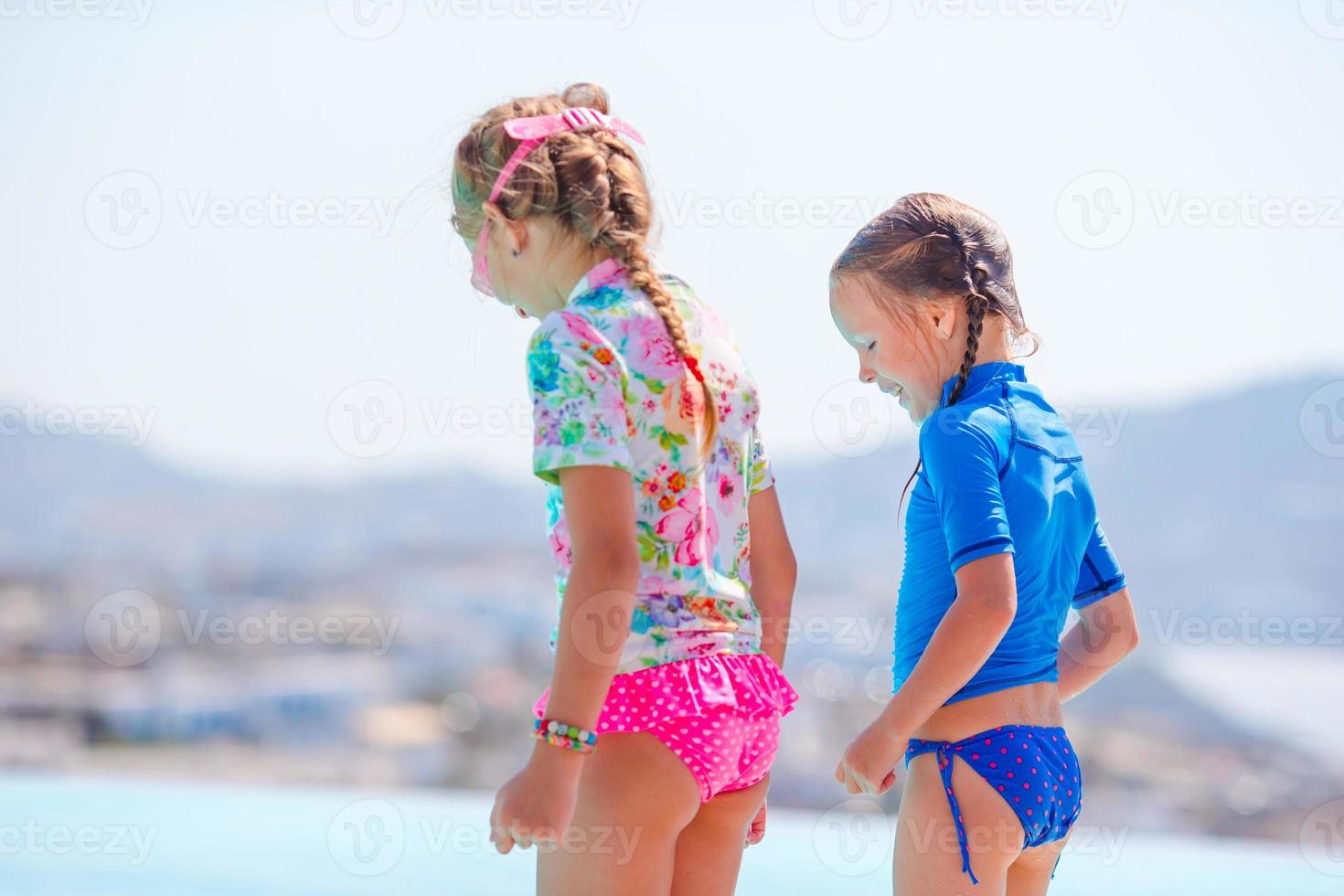 Adorable little girls on the edge of outdoor swimming pool with beautiful view photo