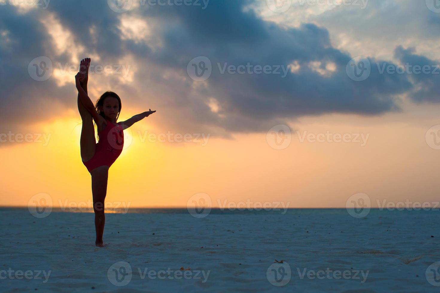 Silhouette of adorable active little girl on white beach at sunset photo