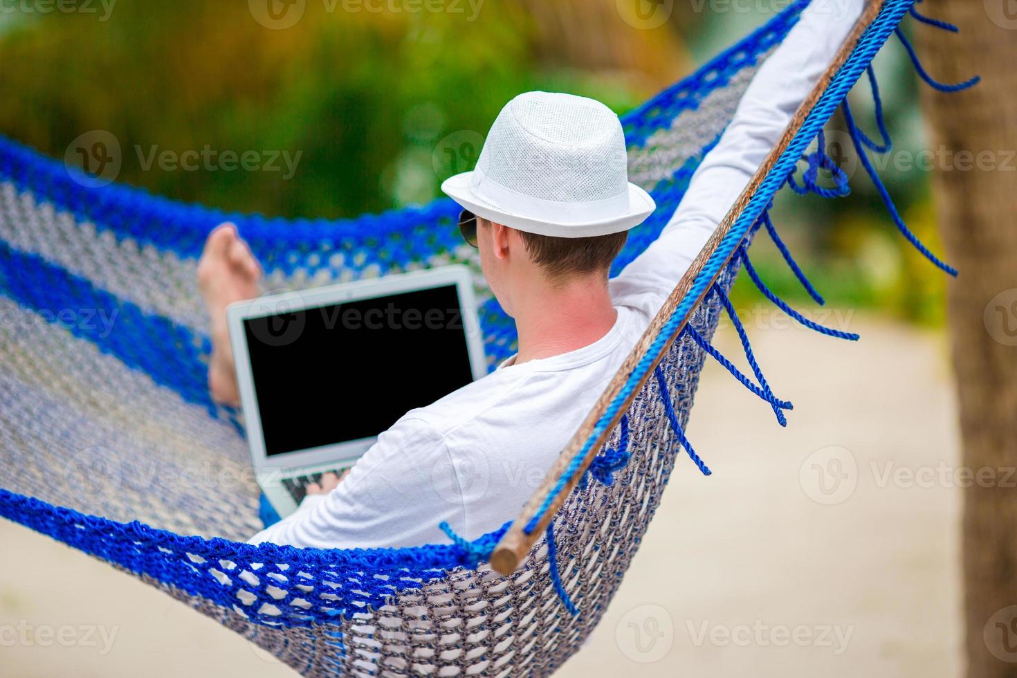 Young man with laptop at hammock on tropical vacation photo