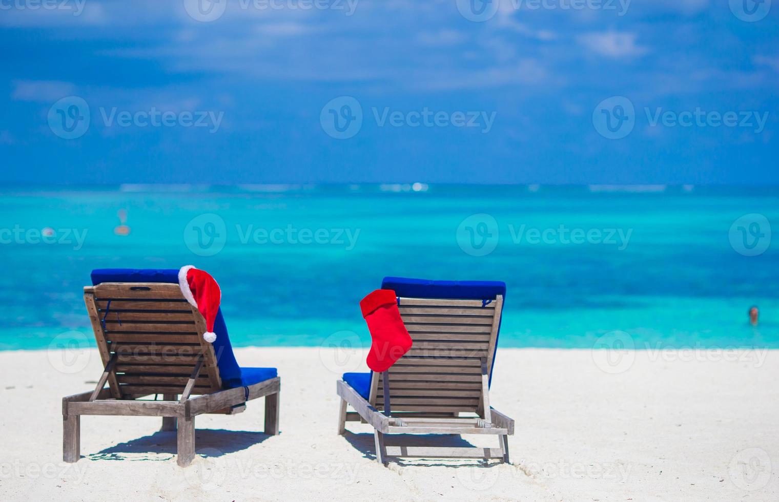 Red Santa Hat and Red Christmas stocking on beach loungers on tropical vacation photo
