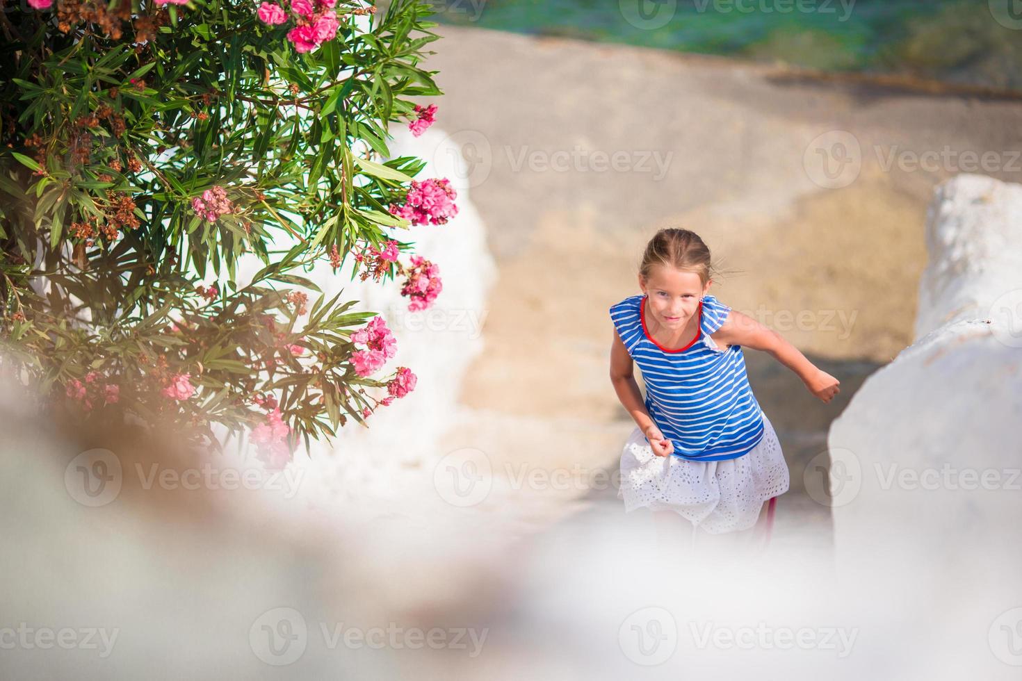 Adorable girl having fun outdoors. Kid at street of typical greek traditional village with white walls and colorful doors on Mykonos Island, in Greece photo