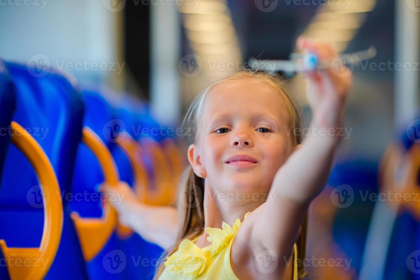 Adorable little girl traveling on train and having fun with airplane model in hands photo