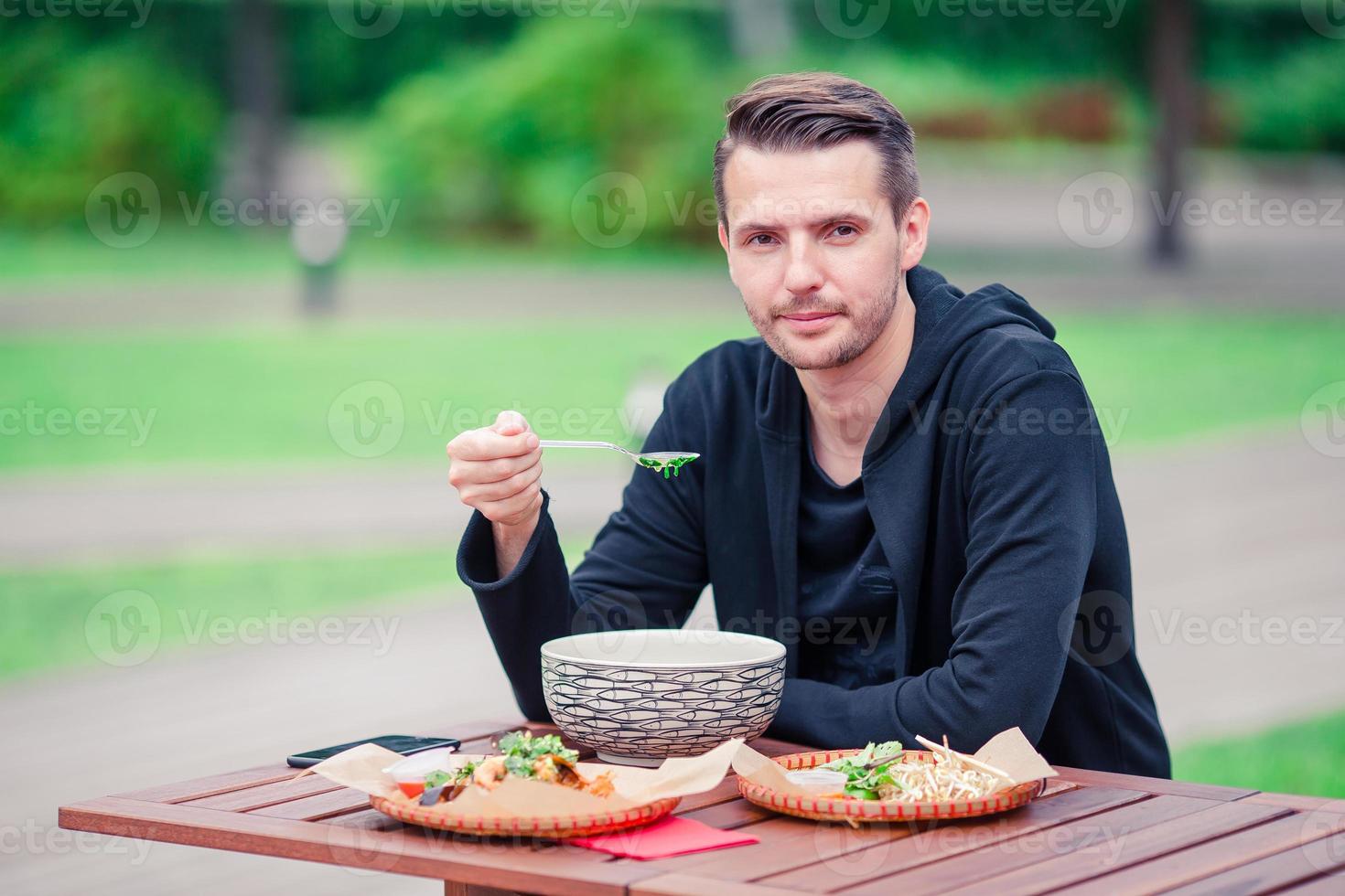 Young man eating take away noodles on the street photo