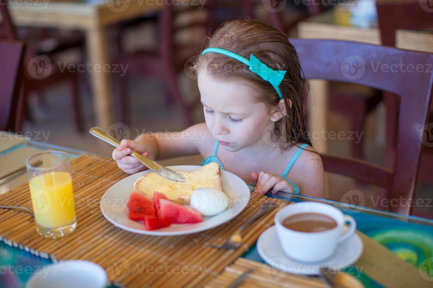 Adorable little girl having breakfast at resort restaurant photo