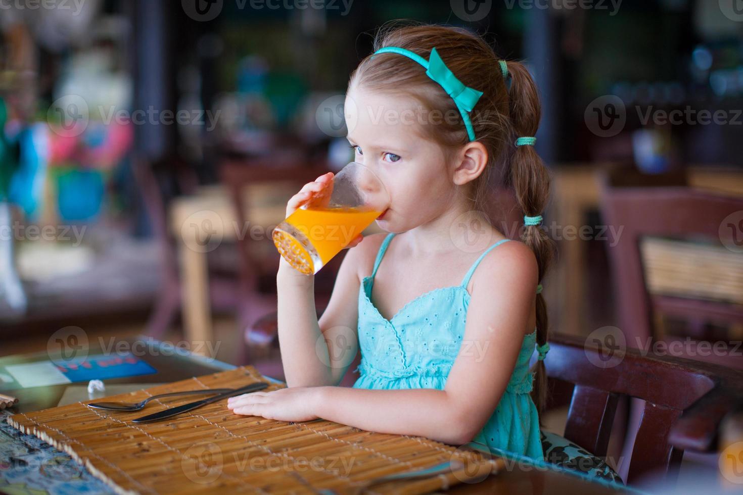 Adorable little girl having breakfast and drinking juice at resort restaurant photo