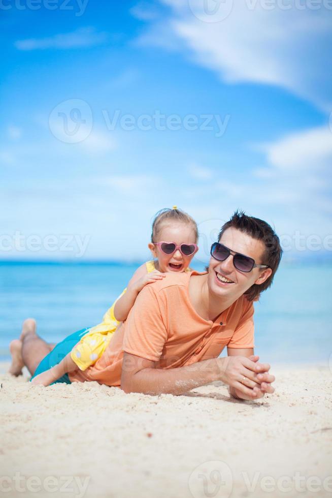 Happy father and his adorable little daughter lying on white sand beach photo