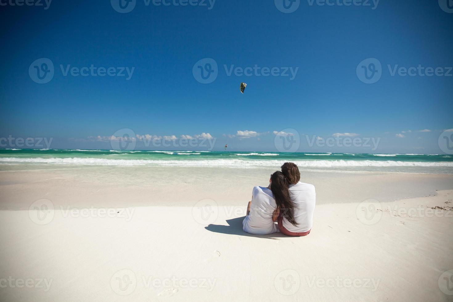 Back view of young couple sitting at tropical white beach photo